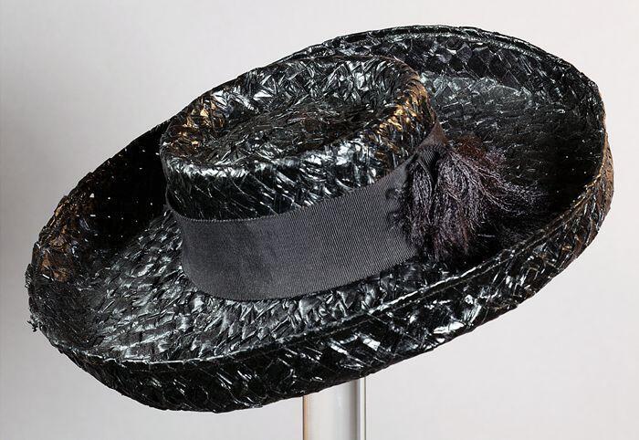Strohoed van zwart raffia met ingedeukte bol waar omheen ripslint en brede hoedrand die rondom iets…