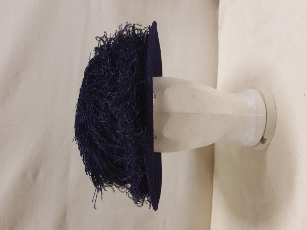 Vrouwenhoed van donkerblauw vilt. Rand van stijf donkerblauw riet. Donkerblauwe struisveren