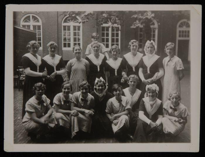 Zwart-wit foto van een groep weesmeisjes van het Gereformeerd Burger Weeshuis, een deel gekleed in…