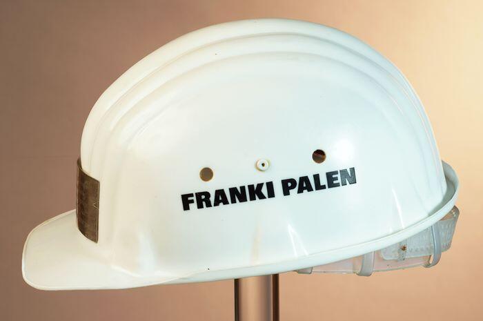 Witte veiligheidshelm met "FRANKI PALEN" en zilveren plaat met "... Stadstimmerhuis, …