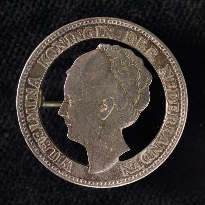 Draagspeld, bestaande uit zilveren gulden, waarvan het contour van Koningin Wilhelmina is uitgezaagd