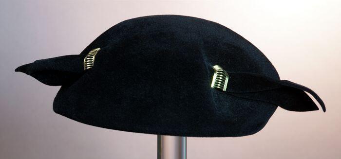 Ronde baret, zwart vilt met garnering van twee goudkleurige halve ringen en zwart vilten stijve…