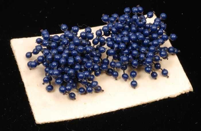 Paar oorbellen, clip met donkerblauwe plastic bolletjes op draad, op wit karton, kapper Van Vliet