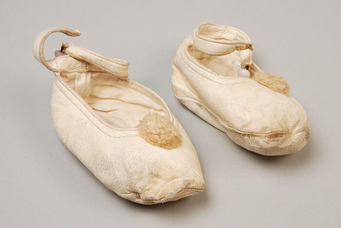 Witte leren babyschoentjes met wollen pompoentje op de neus en enkelbandje met knoopsluiting