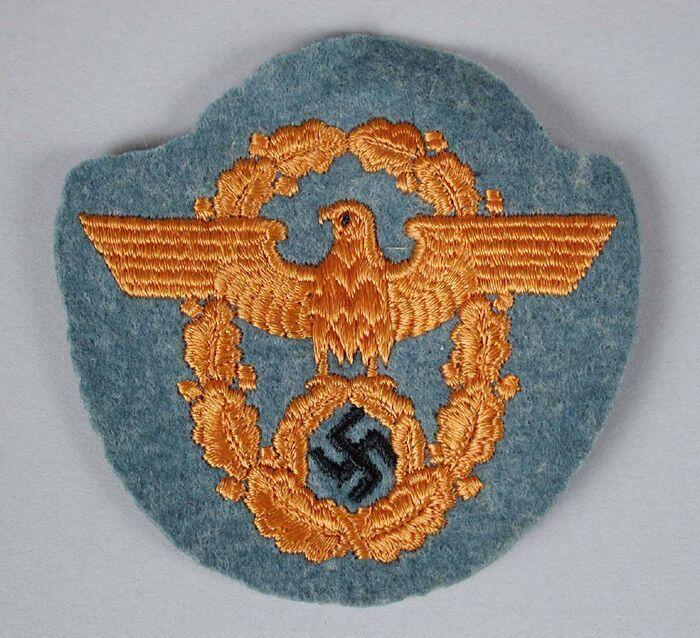 Stoffen embleem van grijs vilt met oranje geborduurde Rijksadelaar binnen een krans met het…