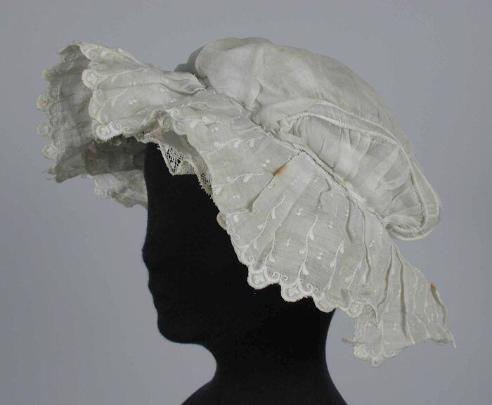 Boudoirmuts van wit glasatist, ingerimpelde delen opzij, brede geplooide broderie ruche rondom,…