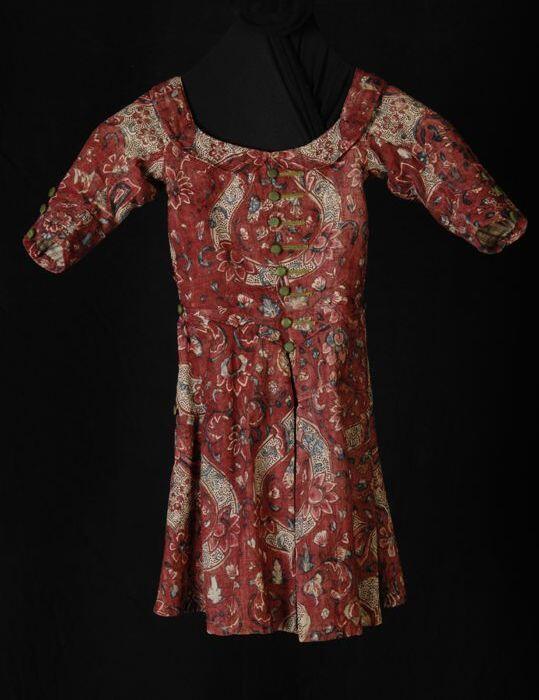 Kinderjurk van linnensits, roodbruin fond met bloemmotieven in wit en blauw, wijde hals met platte…