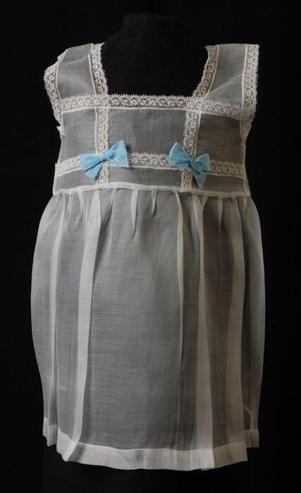 Babyjurk, mouwloos schortmodel van transparant wit nylonmet lichtblauwe strikken en wit kant, …