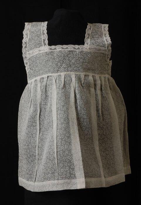 Babyjurk, mouwloos schortmodel van transparant wit nylonmet bloemmotief, 'Femifra' model 'Connie'