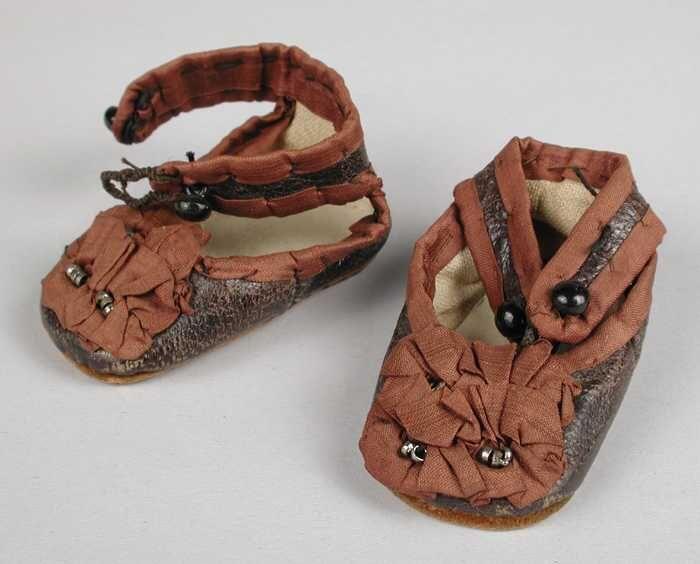 Paar miniatuur zwart leren schoenen met enkelband, randen met roodbruin zijde op de voet geplooid…