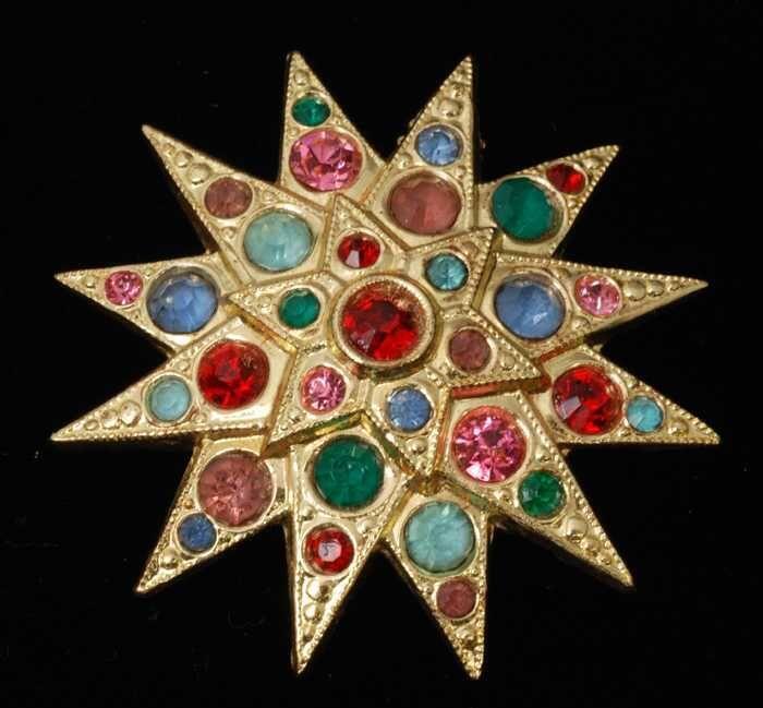 Broche, twaalf-puntige ster van goudkleurig metaal met veel gekleurde kunstdiamantjes, kapper Van…