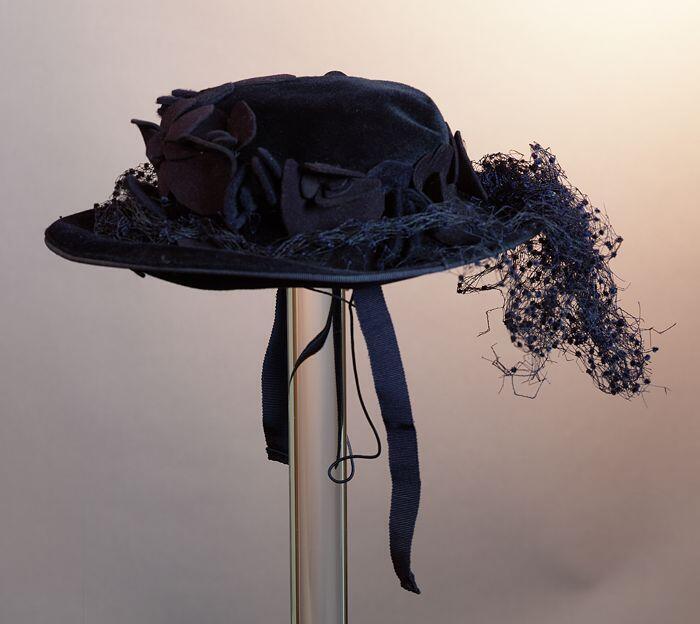 Ronde meisjeshoed van donkerblauw velours, garnering donkerblauw vilten bloemen en nopjes voile…