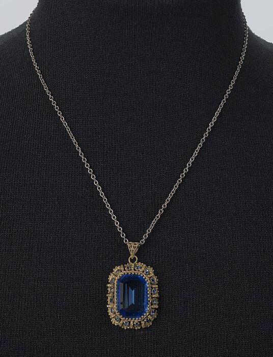 Halsketting van zilverkleurige schakeltjes met een rechthoekige sierhanger van facetgeslepen blauw…