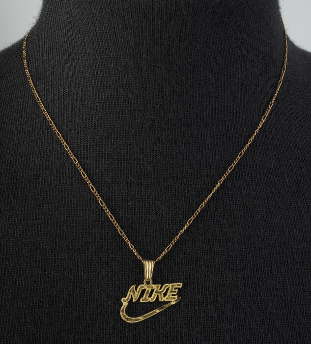 Gouden hanger in de vorm van het "Nike"-logo aan gouden schakelketting met fantasieschakels