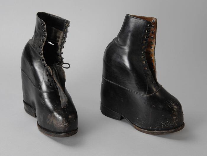 Twee orthopedische (linker-) schoenen van glad zwart leer met een zeer verhoogd voetbed, rijglaars…