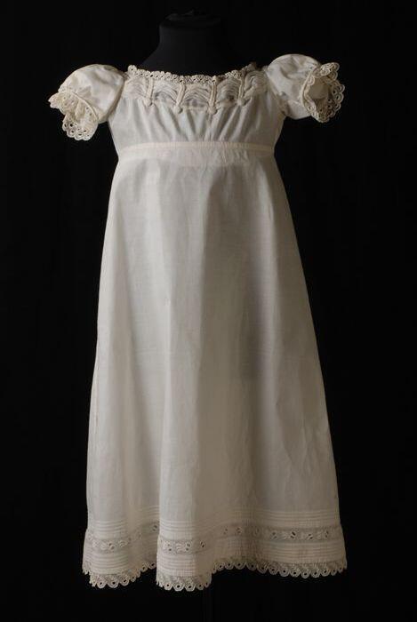 Lange kinderjurk, empire, van wit katoenen mousseline langs de hals met sierknopen, broderie…