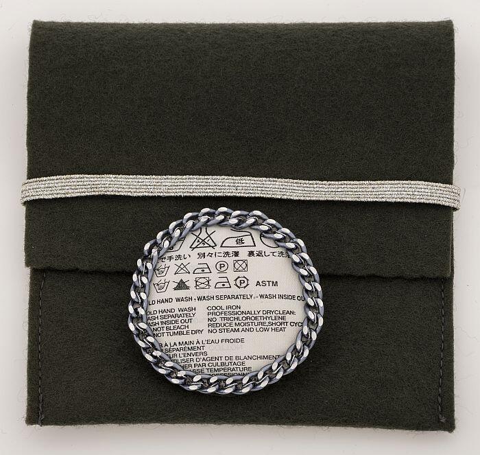 Ronde broche van wasetiket ('Care instructions'), met klein grijs etui