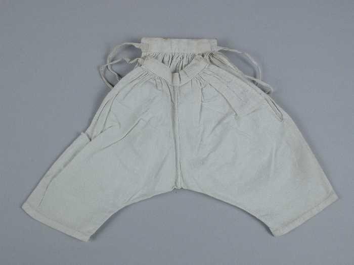 Poppenonderbroek van wit katoen met halflange pijpen, strikbanden in de taille