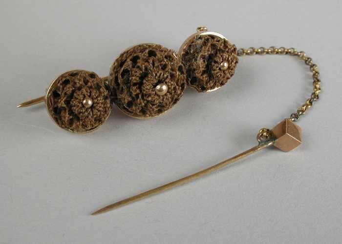 Gouden broche met sierspeld aan kettingje, en drie gevlochten knoopjes van haar
