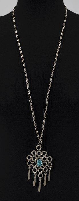 zilverkleurige metalen schakelketting met hanger van metalen vlechtwerk met daarop turkoise…