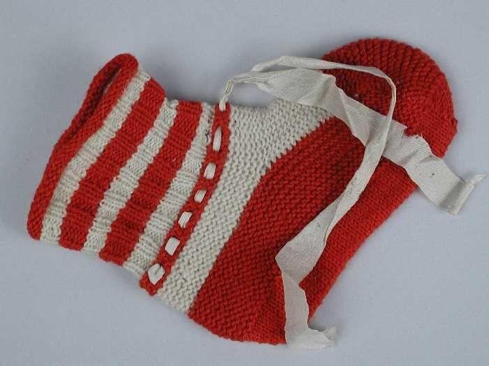 Paar babysokken gebreid van rode en witte wol in tricot- en ribbelsteek, wit zijdelint door de enkel
