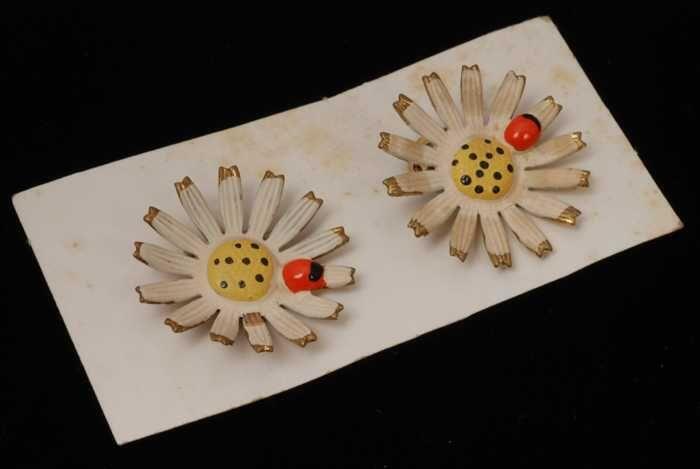 Paar oorbellen, clip met bloem van metaal, wit met geel hart en rood kevertje, op wit karton,…