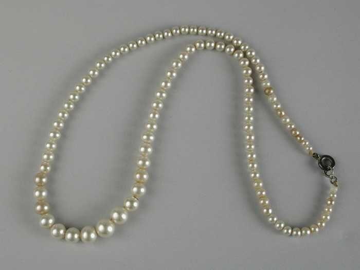 Parelsnoer, ketting van parels, bij de metalen sluiting kleine pareltjes, naar het midden toe…