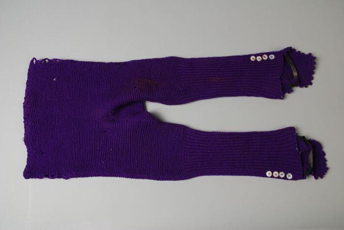 Kinderslobbroek gebreid van donkere paarse wol parelmoeren knoopjes en zwart elastiek in de taille…