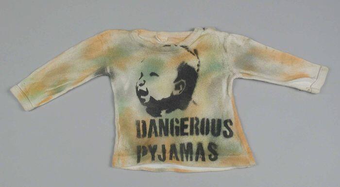 Baby t-shirt van wit tricot katoenbespoten met oranje en groene verf en in zwart "Dangerous Pyjamas"