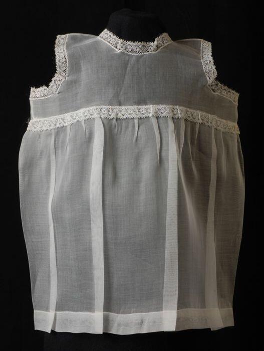 Babyjurk, mouwloos schortmodel van transparant wit nylonmet wit kant, 'Femifra', model "Ineke"