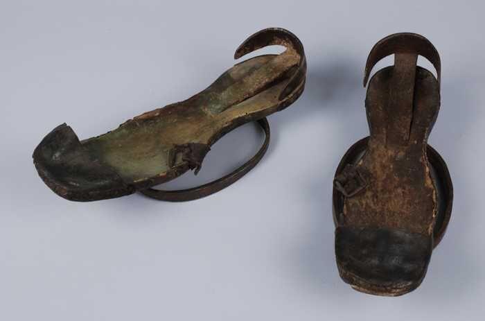 Metalen trippen met houten voetbed, messing hielstuk en leren teenkap, midden onder de voet een…