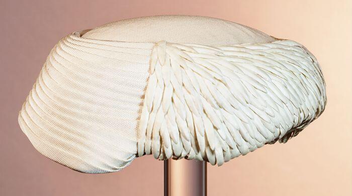 Ronde toque, witte geplooide stof, garnering van imitatieveertjes van witte glanzende stof