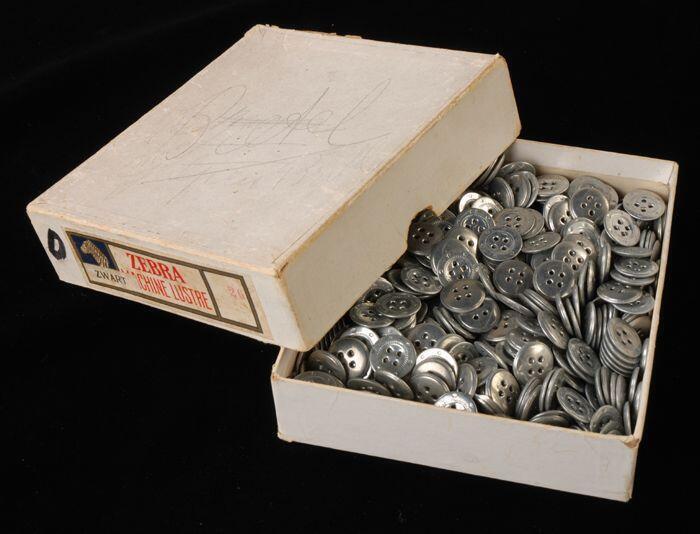 Rechthoekige doos (1) van karton met los deksel (2) waarin veel metalen bretelknopen (3) "Zebra"