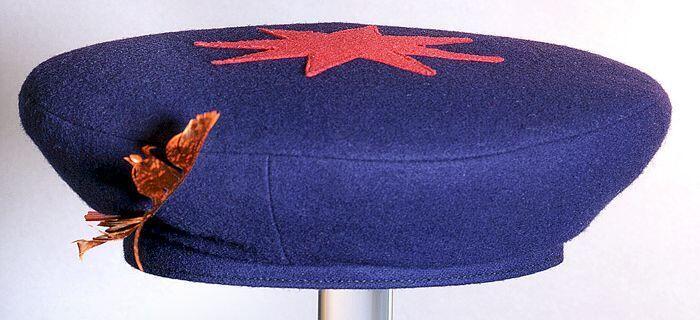 Ronde, donkerblauwe meisjesbaret, met bovenop achtpuntige rode ster en langs de rand een rode veer