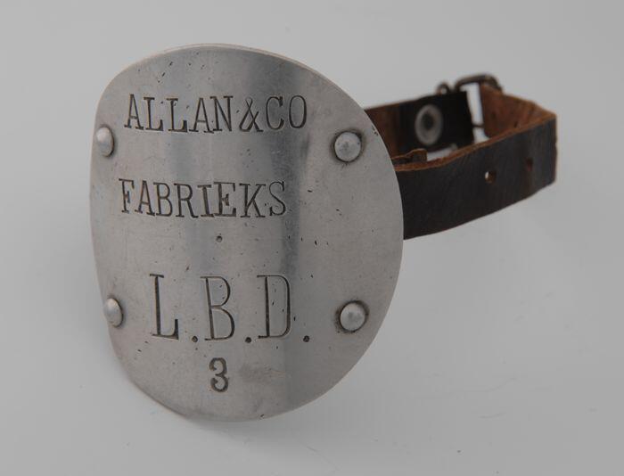 Aluminium mouwembleem met opschrift "Allan & Co Fabrieks L.B.D. 3", bevestigd aan lederen…