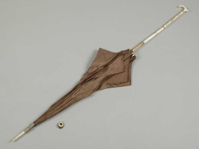 Parasol met bruine bekleding van zijde steel deels van hout deels van bewerkt ivoor, losse ring