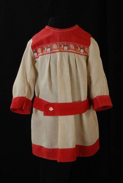 Kinderjurk, schort model van crèmekleurig katoen met rood sierband waarop molens en boer en boerin