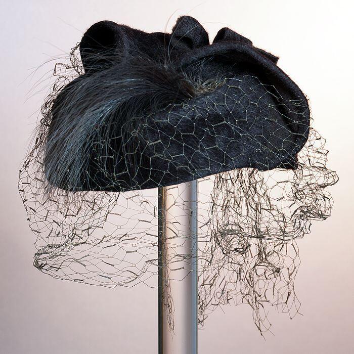 Donkerbruine dameshoed van vilt met flap en strik bovenop, een pluimveer en bruin voile