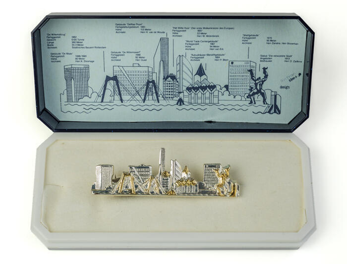 Dasspeld met verzameling Rotterdamse gebouwen in zilver en goudkleur, in donkerblauw kunststofdoosje