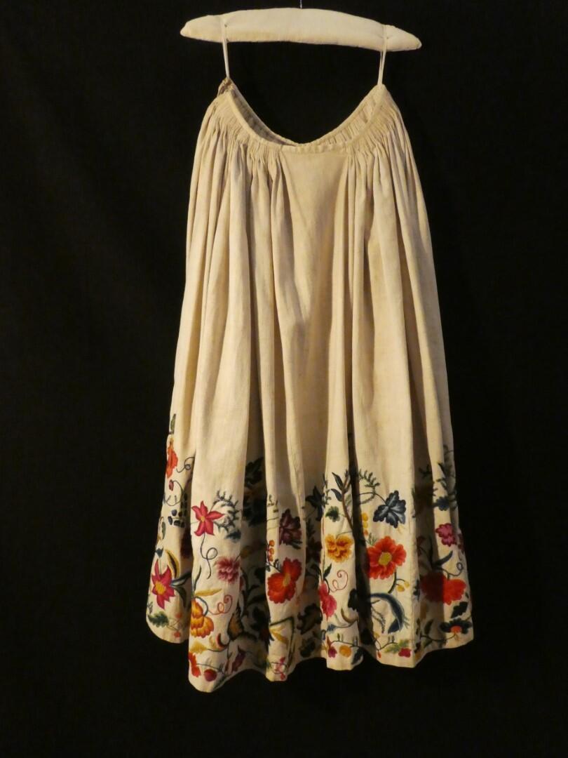 Rok van wit katoen met ingeweven ribbel, aan onderrand crewelwork van bloem- en bladmotieven in…