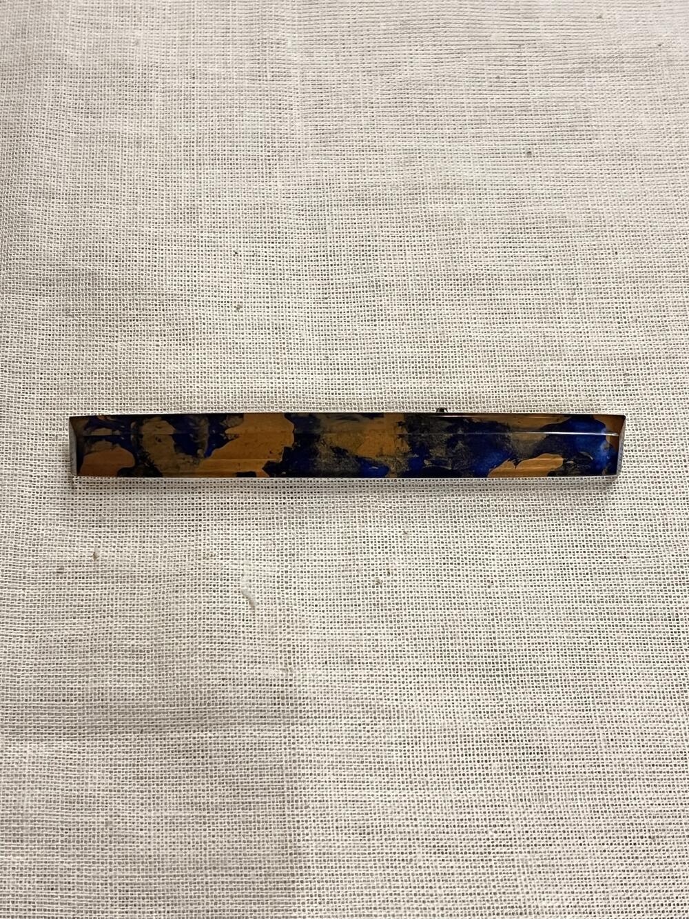 Broche, langwerpige staaf-vorm, koperkleurig en blauw 'wolkerig' effect met doorzichtig kunststof