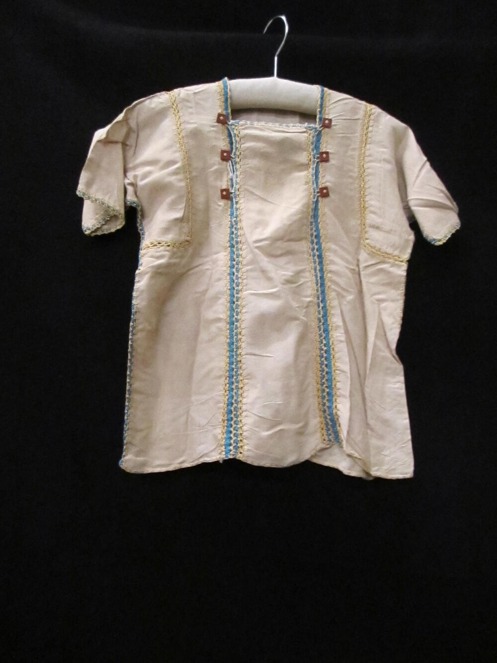 Zomerblouse (kind) van beige katoen, afgezet met haakwerk van blauw en geel katoen. Met haakwerk…