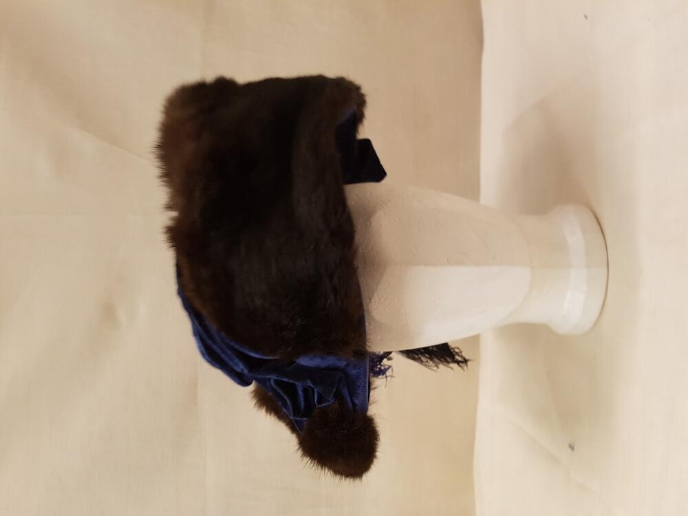 Hoed van helderblauw fluweel, gegarneerd met strook donkerbruin langharig bont en grote struisveren