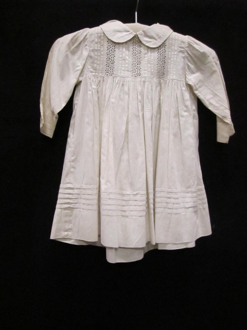 Schort (kind) van wit katoenen piqué met tussenzetsels van machinale broderie