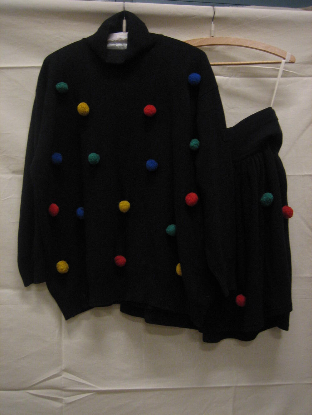 Ensemble bestaande uit trui en rok van zwarte gebreide wol met pomponnetjes in blauw, rood, geel en…