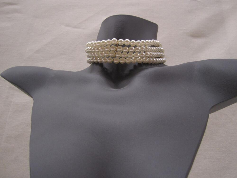 Ketting bestaande uit 4 rijen witte parels, welke onderbroken worden door 3 goudkleurige plaatjes