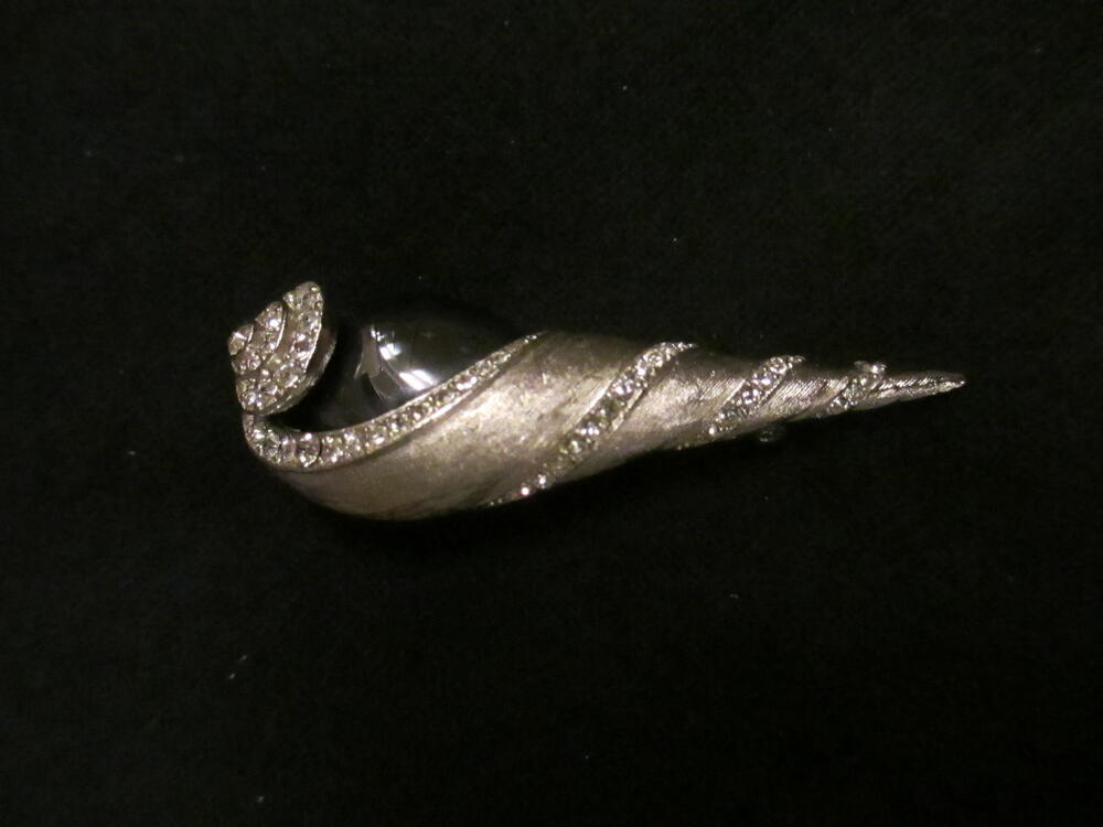 Broche, schelpvormig model van zilverkleurig metaal bezet met witte strass-stenen en druppelvormige…