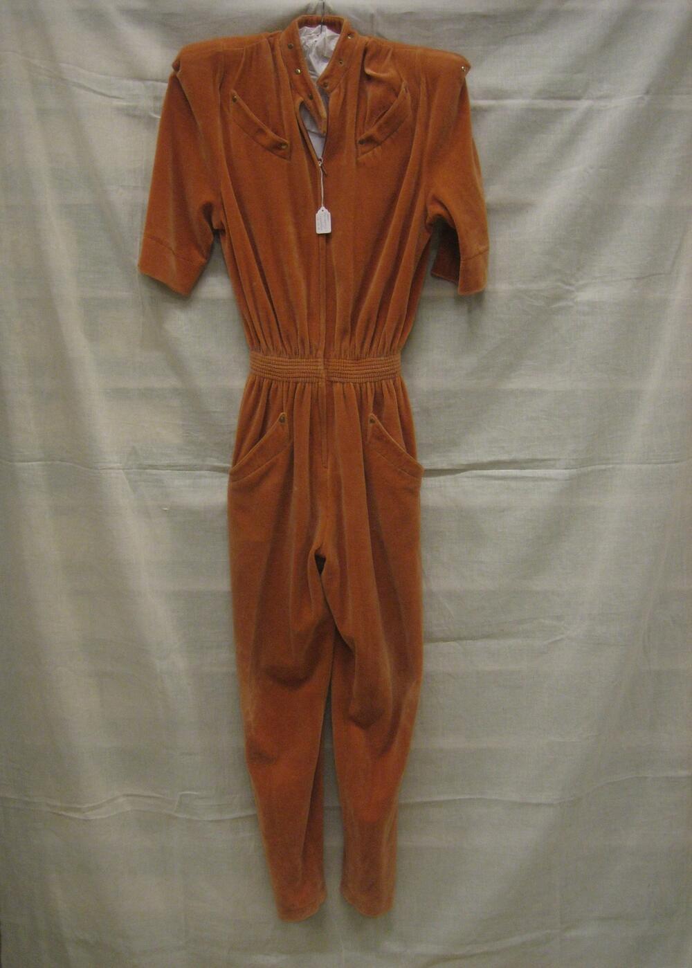 Jumpsuit van oranje-bruin fluweel, korte mouw, smalle pijpen en brede schouders