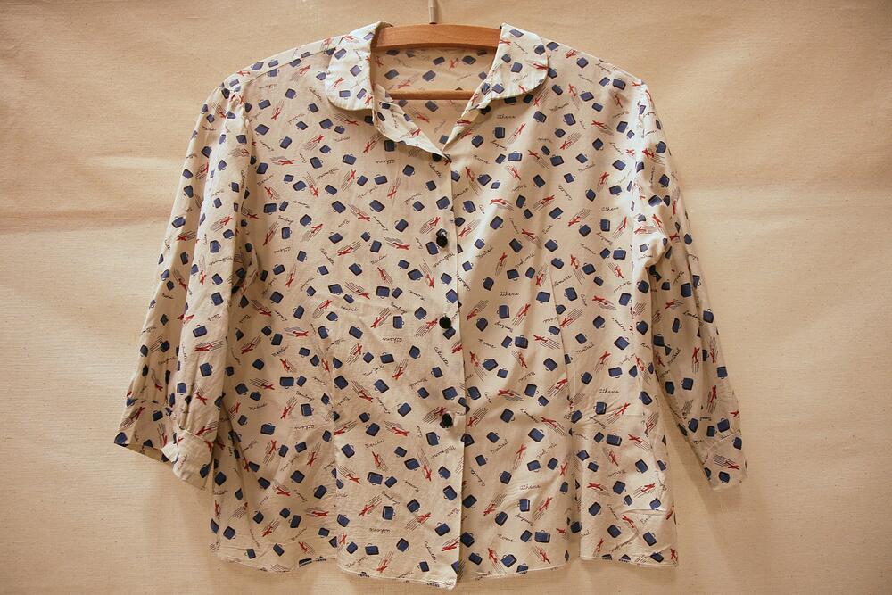 Blouse van crêmekleurige kunstzijde met bedrukt patroon van blauwe koffers, rode vliegtuigen en…