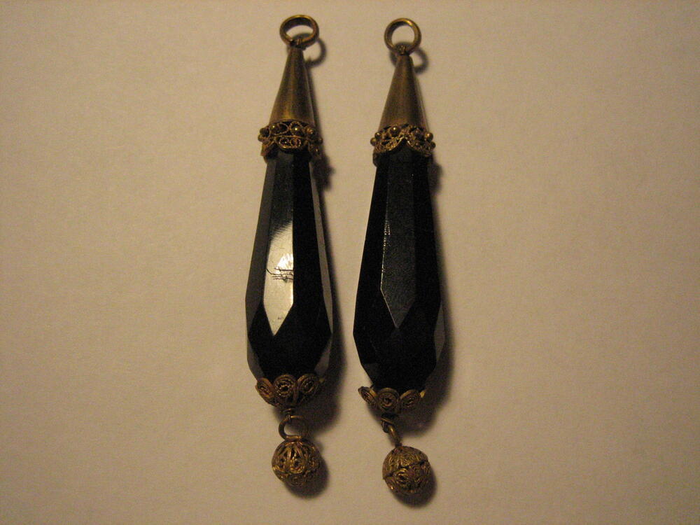 Een stel rouwklokken. Peervormig zwart glas, gevat in kegel. Van onderen ornament met opengewerkt…